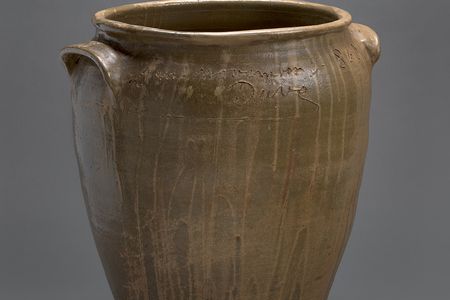 A brown, ceramic vessel with an inscription and the artist's name "Dave" carved around the opening.