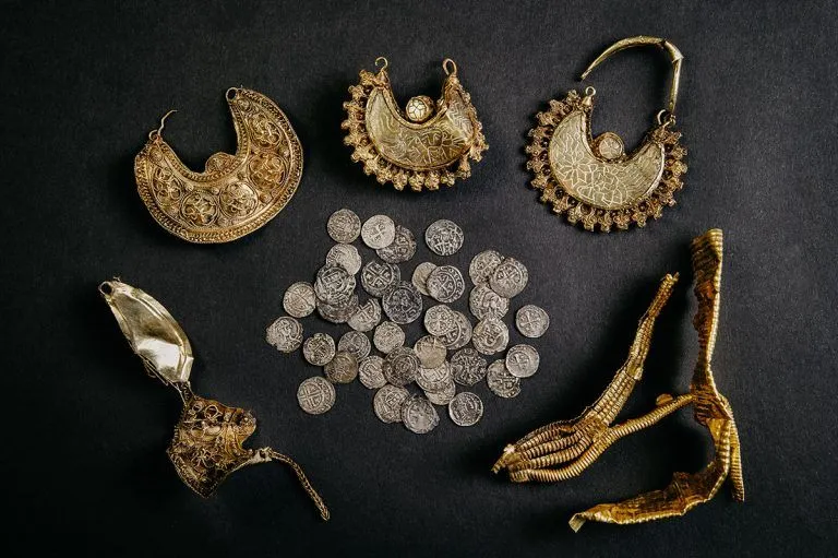 Black background with gold earrings, silver coins and gold leaf