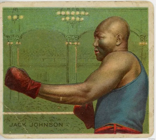 A playing card on which a man wearing boxing clubs in a fighting stance stands against a green background made to look like a large hall with many seated people. He is identified as Jack Johnson by text in the corner.
