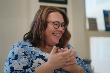 Teacher with short brown hair and glasses, wearing a blue shirt is smiling and clapping