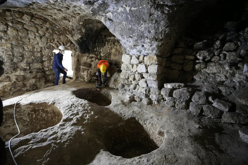 Two workers in a large chamber with a number of pits