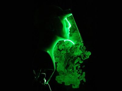 Green lasers pointed at a plastic mannequin head wearing a face shield show how the droplets from a cough or sneeze escape around the sides. 