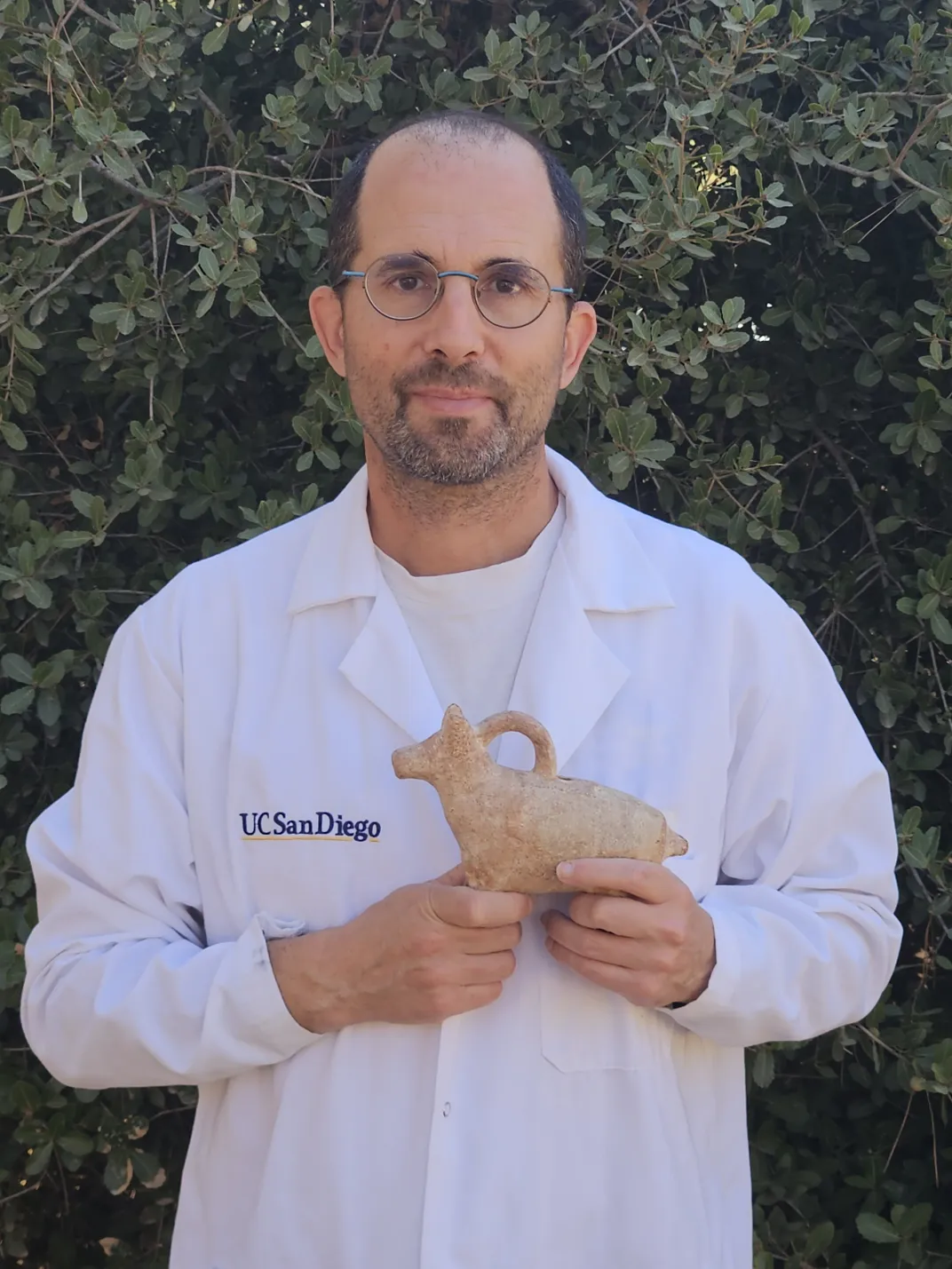 Researcher Yoav Vaknin wears a lab coat and holds an animal figurine