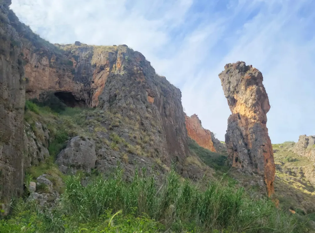 Landscape with green grass and rock formations against blue sky