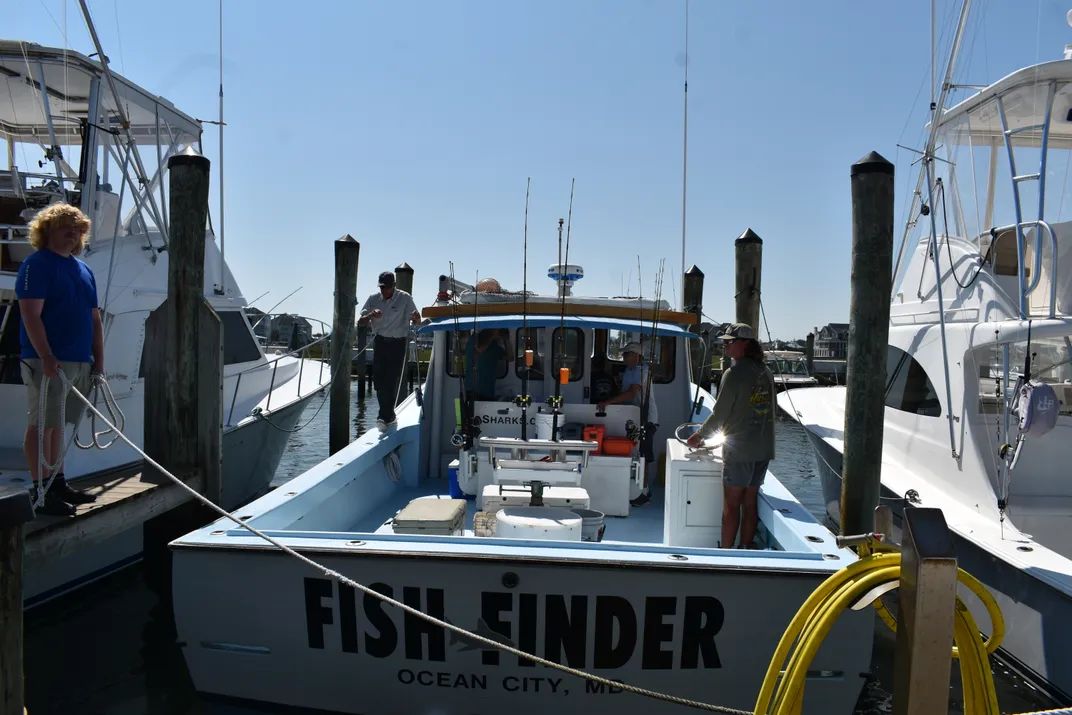a boat with the words "fish finder" at dock and some people getting ready to board it