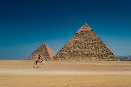 A man rides a camel in view of the remarkable Egyptian pyramids.