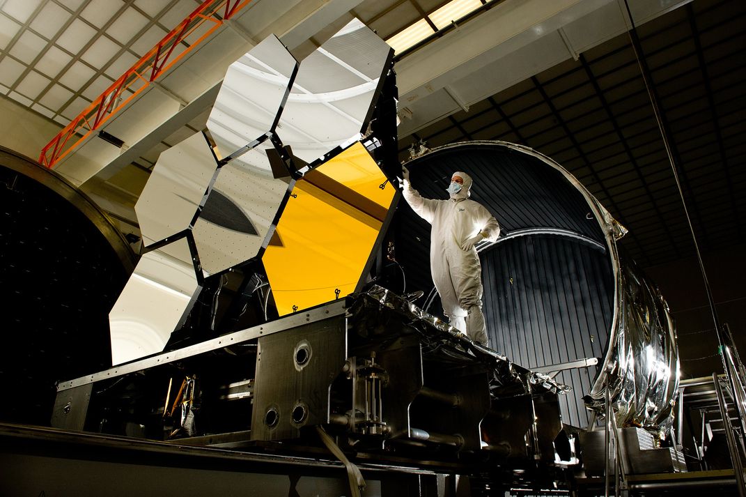 an engineer reaches toward Webb's hexagonal mirrors on a platform