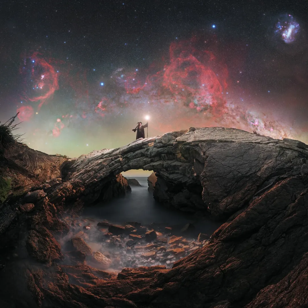 a wizard standing over a natural rock arch over water with a starry sky in the background