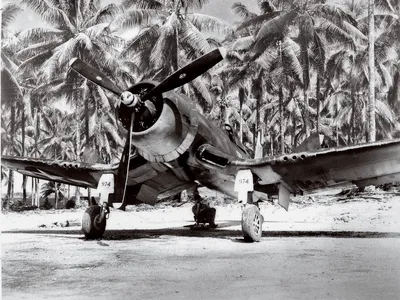 A VMF 222 Corsair catches some rays on Green Island while a ground crewman catches up on his reading.
