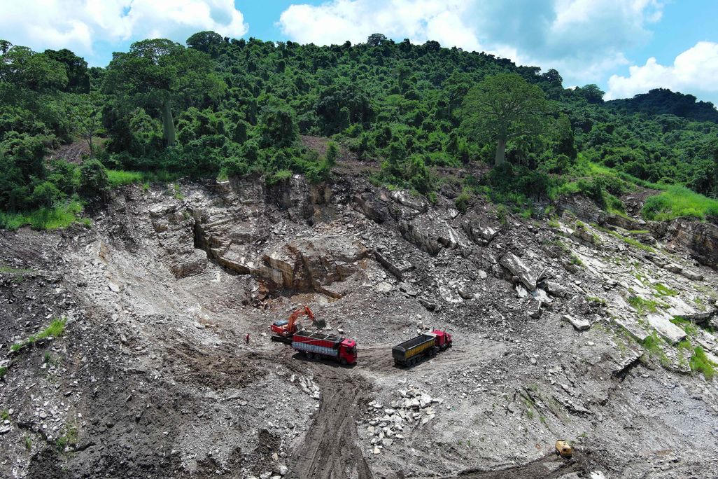 two trucks on rocky ground in front of lush trees