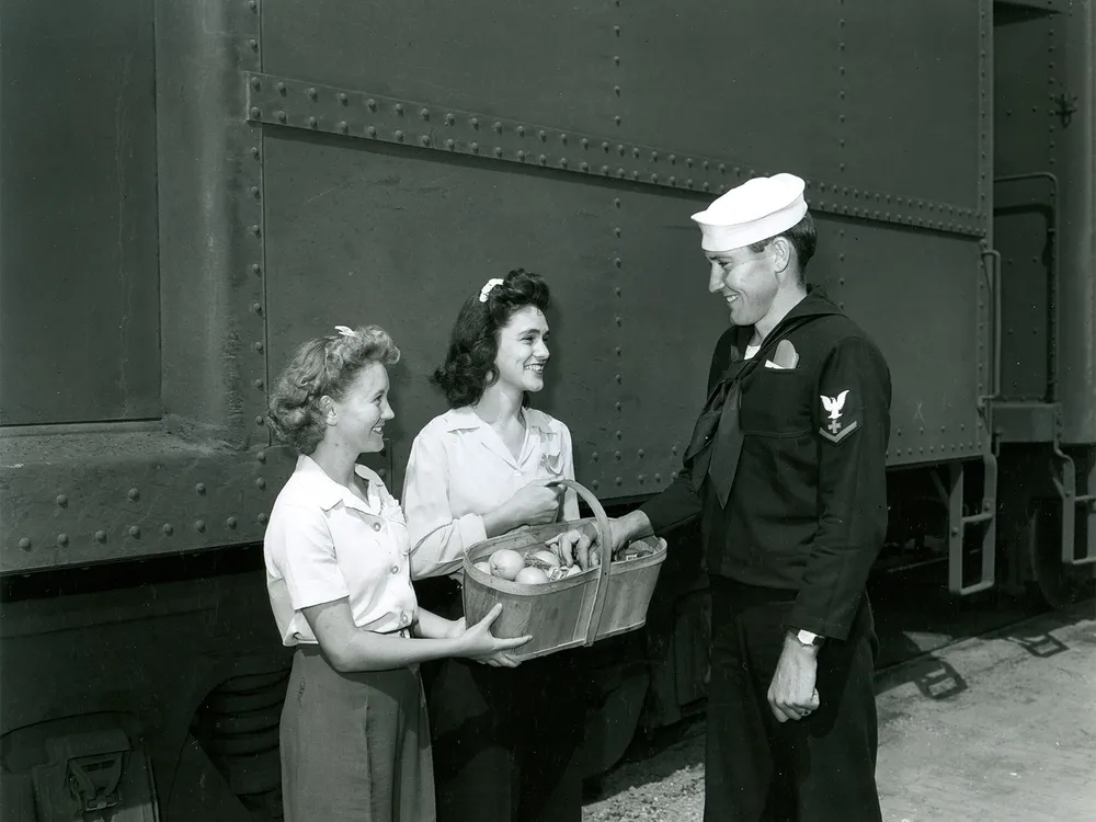 Two canteen volunteers offer a basket of food to a soldier