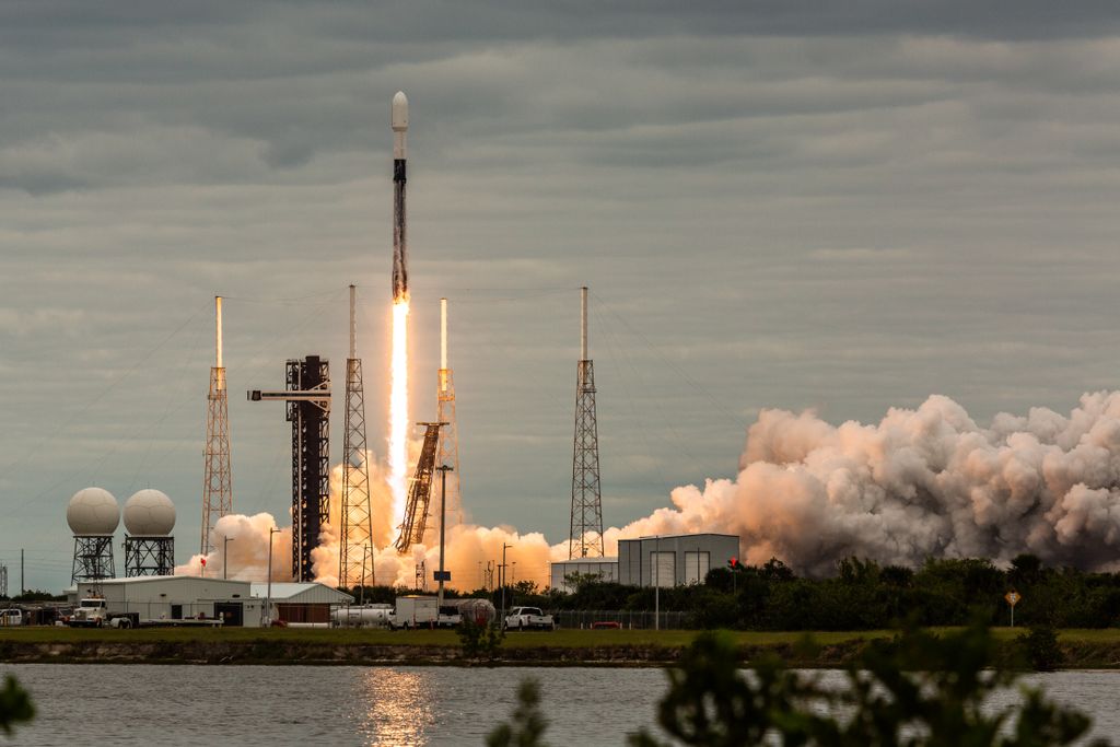 rocket launches with a cloud of smoke beneath it and water in the foreground