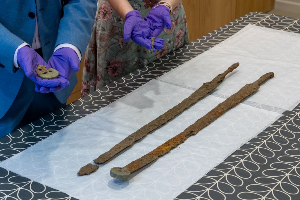 Pair of gloved hands next to long skinny swords