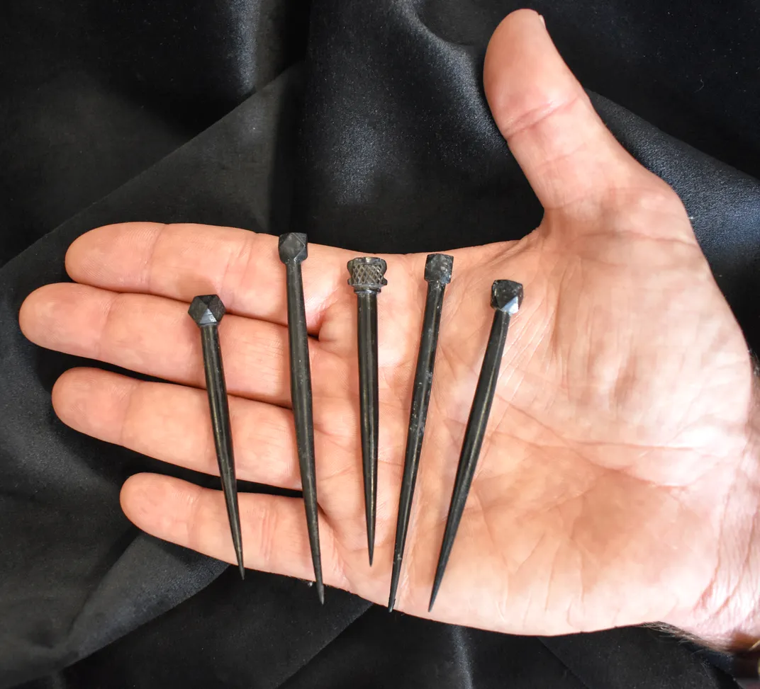 A person's hand holding five sharp hair pins