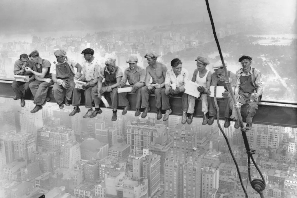 11 men sitting on a beam eating lunch above New York City