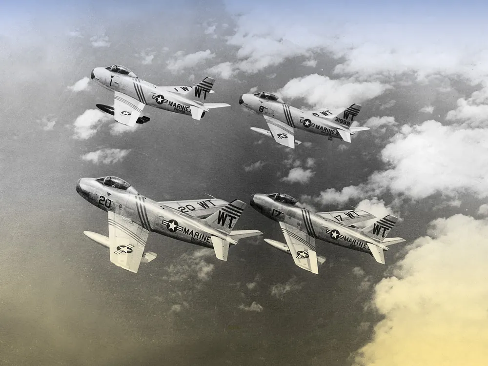 Four vintage fighter jets flying in a tight "finger-four" formation above a thick layer of white clouds in a black and white photograph.
