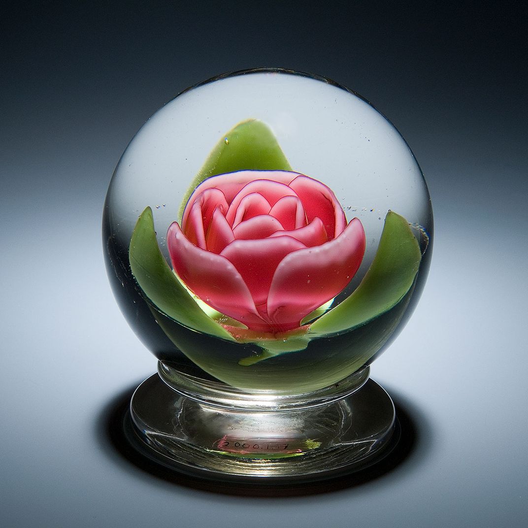 A glass orb with a pink rose and three green leaves designed in the center.