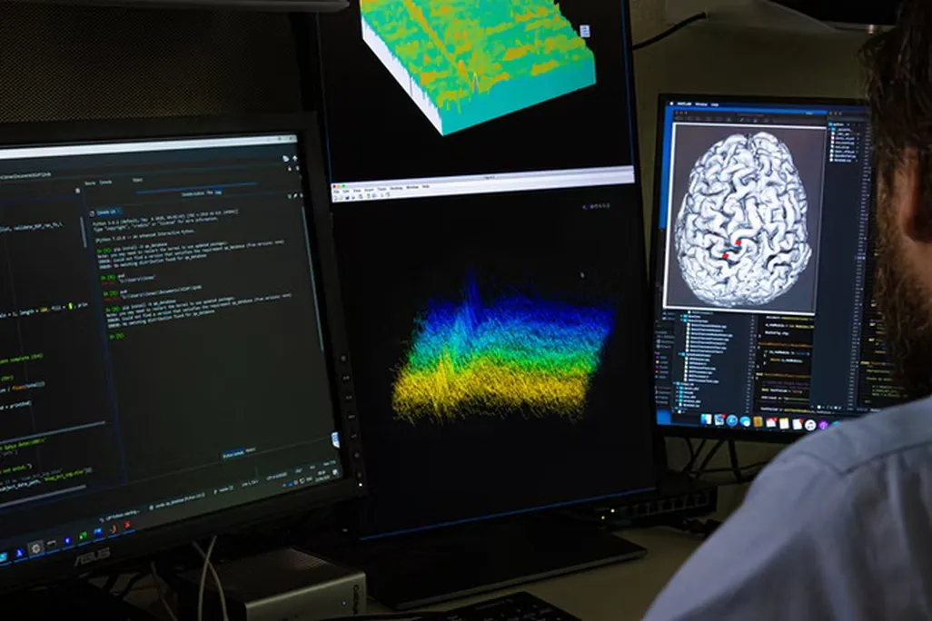 A person sitting in front of screens, one showing a brain