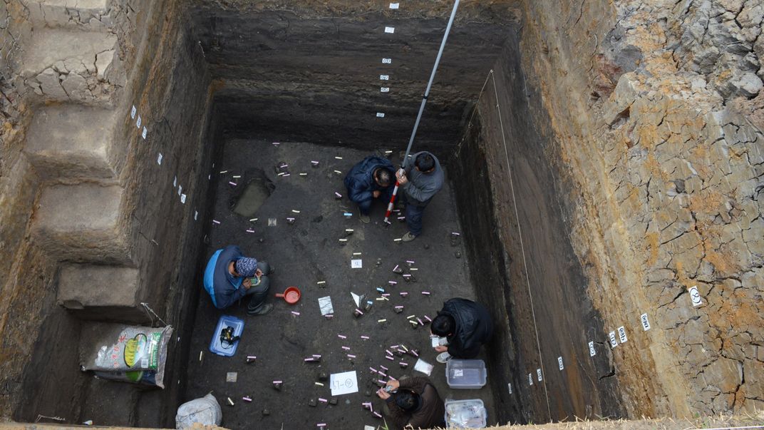 an archaeological trench with people at the bottom