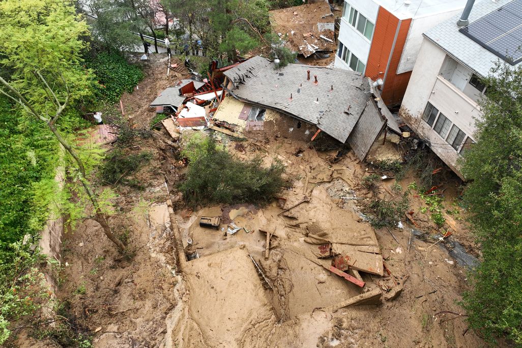 Mud covers land where a house used to be. The house is pushed over and flattened by the mud.