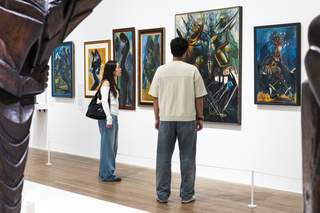 Two people look at a wall of paintings
