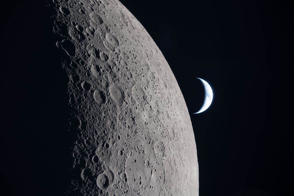 A crescent Earth floats beyond the moon on a dark background