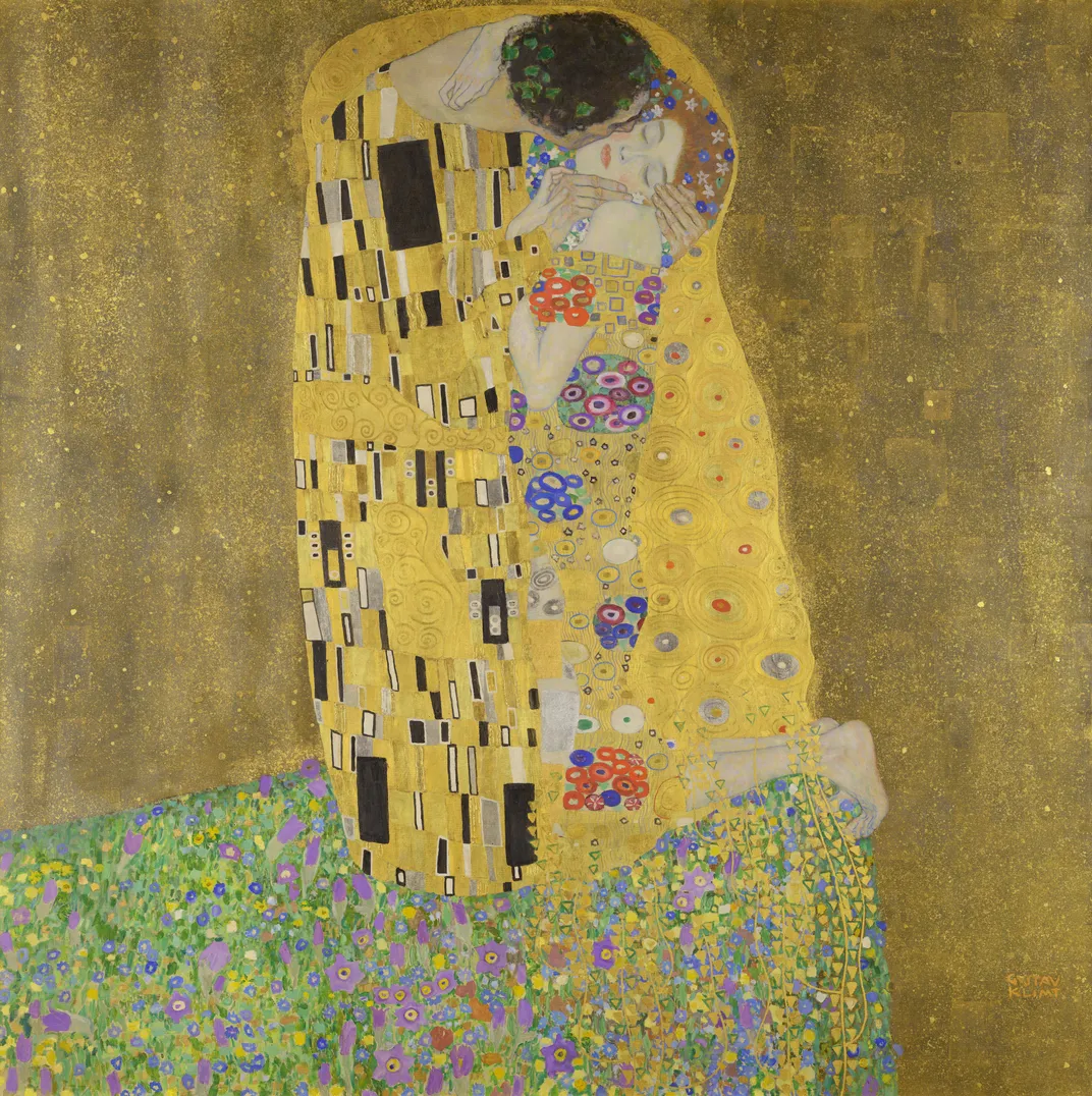 A man and woman in strange geometric garb stand on a field of flowers in front of a golden sea, embracing
