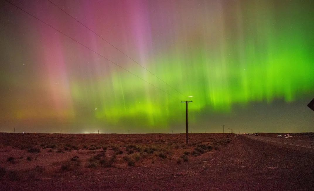 green and red light forms bands, with red on top, over a landscape with a telephone pole