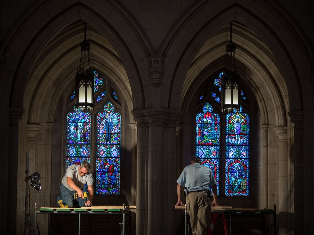 Workers erect scaffolding near two tall stained glass windows, which shine with blue light