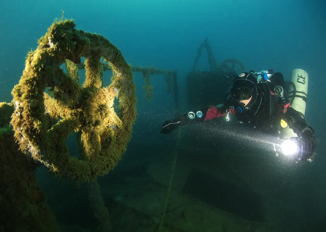 A diver directing a flashlight at what appears to be the wheel of a ship underwater