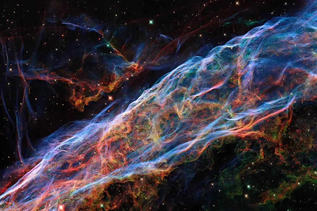 An astronomical image of the Veil Nebula. It is shown in various interweaving filaments of color. 