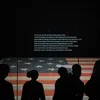 Visitors look at the Star Spangled Banner. It is dimly lit in its gallery at the museum.