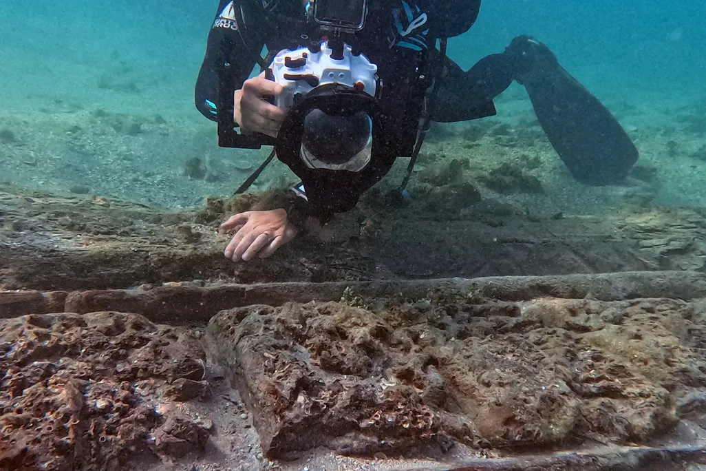 A diver holding a camera while inspecting a shipwreck