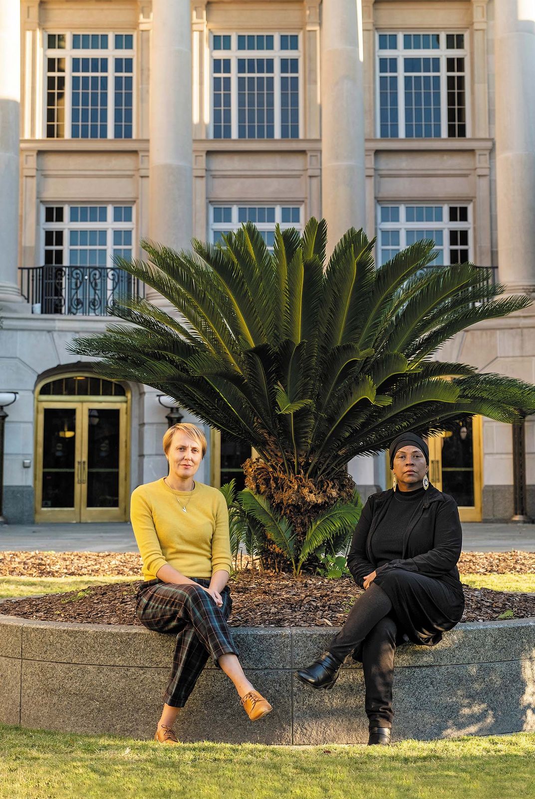 two women sit for a portrait in front of a building