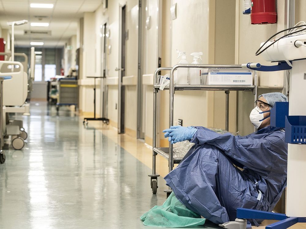 A female doctor wearing protective equipment sitting on the floor of a hospital hallway in Italy