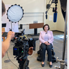 Annamarie Lusardi, seated in a chair facing a camera and lighting equipment.