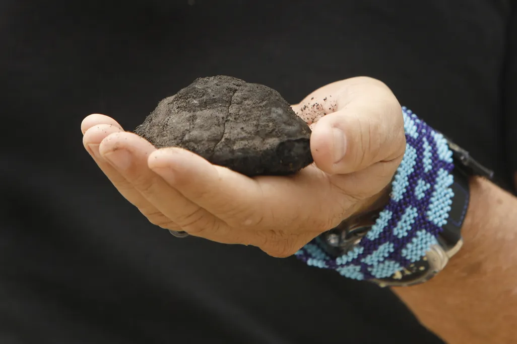 a hand holds a dark lump of metal that looks like a rock