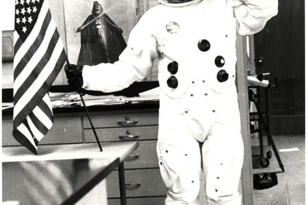 Informal classroom portrait of teacher Herbert Stephen Desind (1945-1992), wearing a reproduction Apollo-era spacesuit, holding an American flag; circa 1980s.  Desind was a space flight aficionado, and his collection of photographs of aircraft and spacecraft was donated to the National Air and Space Museum in 1997. This image is part of the Herbert Stephen Desind Collection.