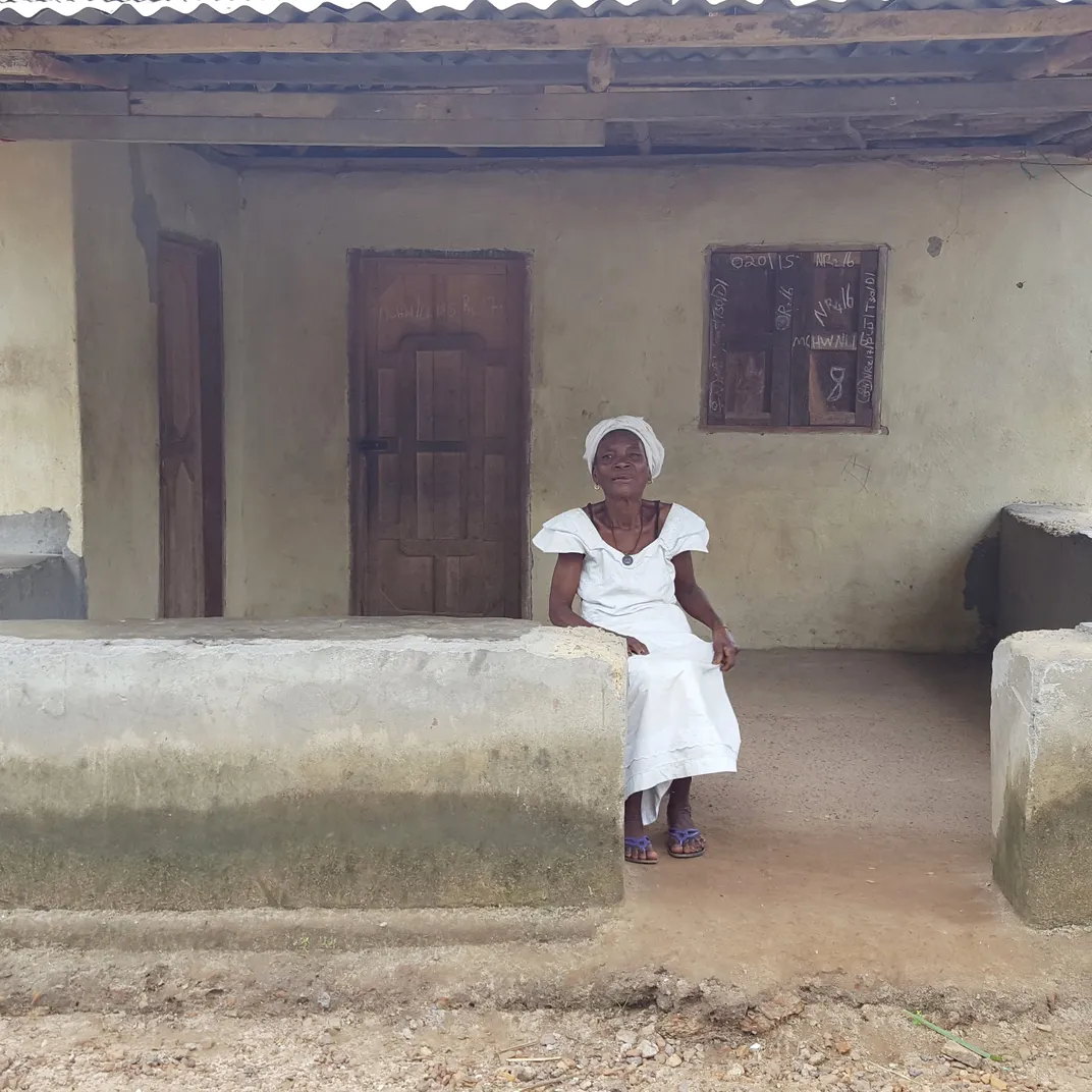 A elderly African woman sits outside her house