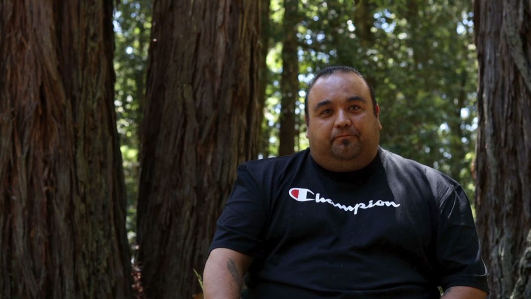 Jesse Gonzalez in a forest. He wears a black Champion-brand T-shirt