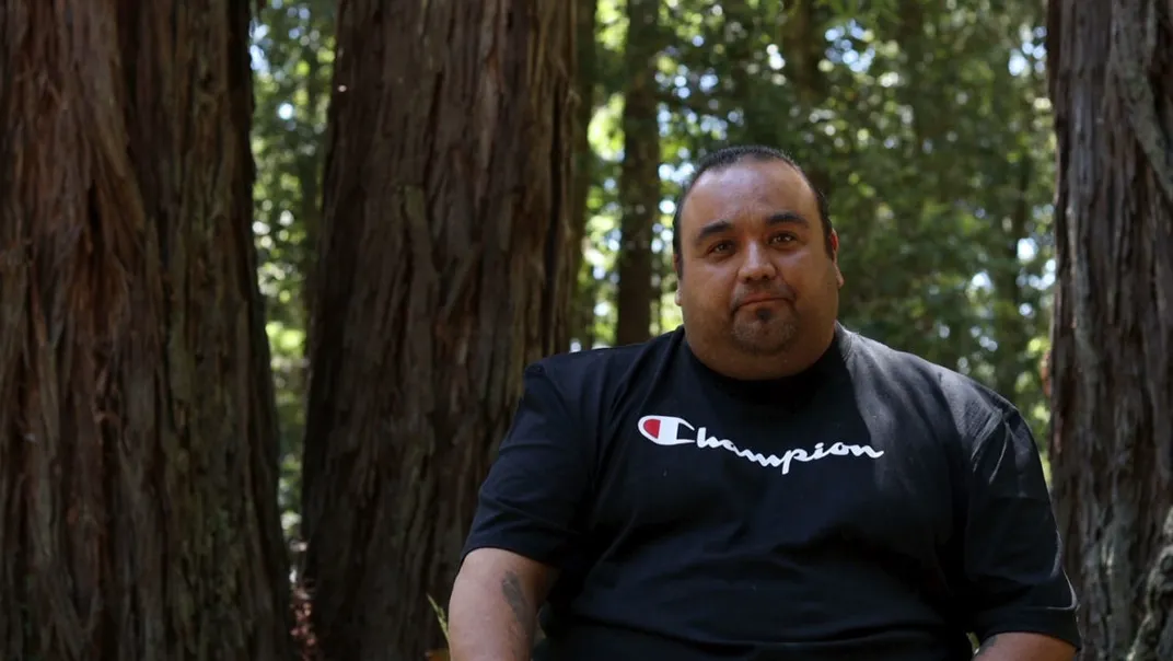 Jesse Gonzalez in a forest. He wears a black Champion-brand T-shirt