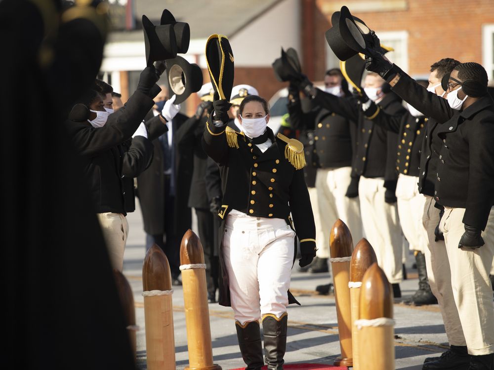 woman in black navy dress uniform being saluted by two rows of fellow sailors