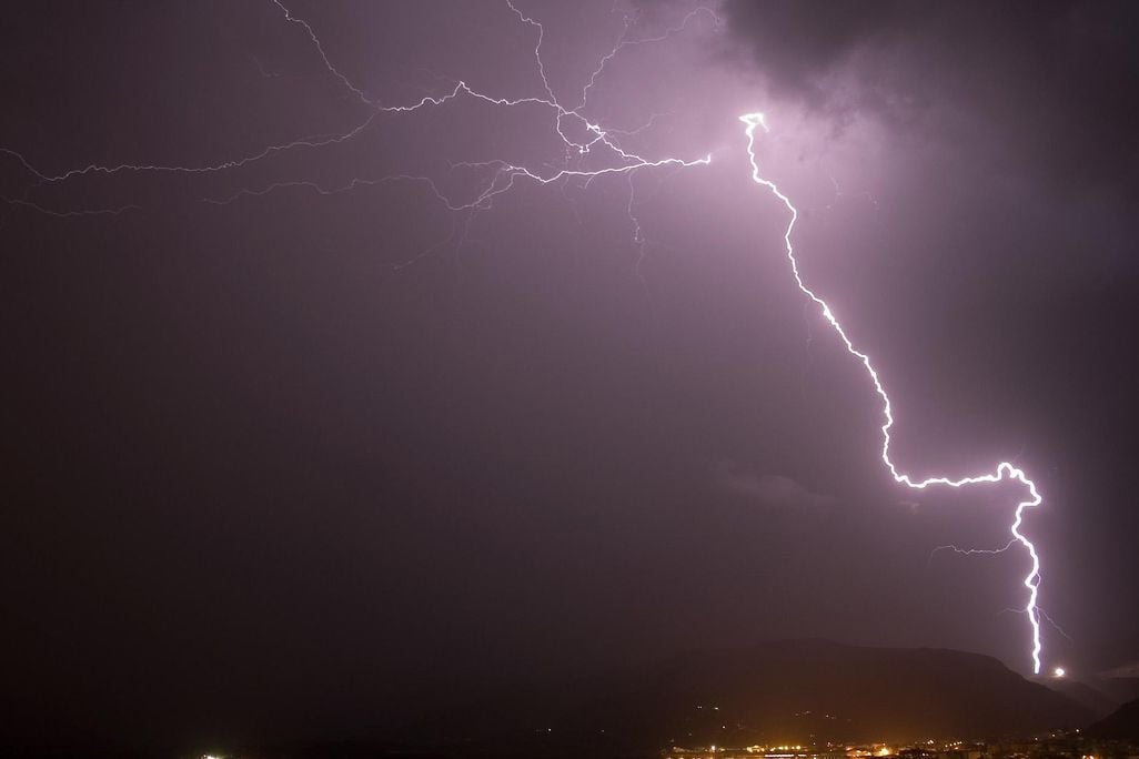 A lightning bolt shoots across the sky at night over a town with yellow lights
