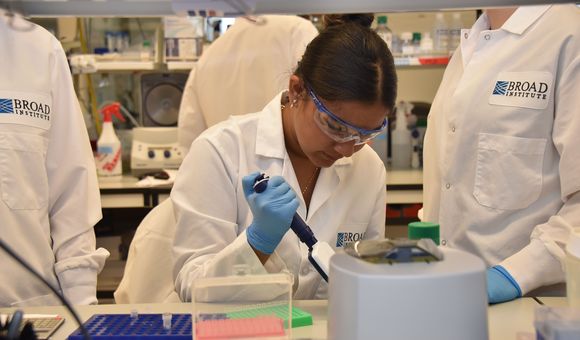A young girl wears a lab coat, safety goggles and blue latex gloves in a research laboratory
