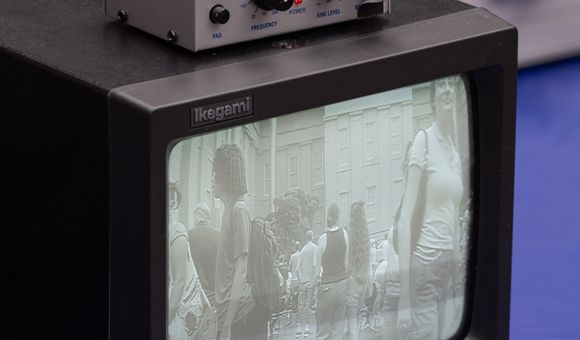 A small black and white tv monitor displays a fuzzy image on the screen. On top of it sits a box with nobs.