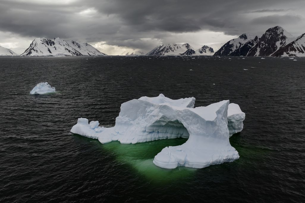 An iceberg sits in the ocean, with mountains in the background