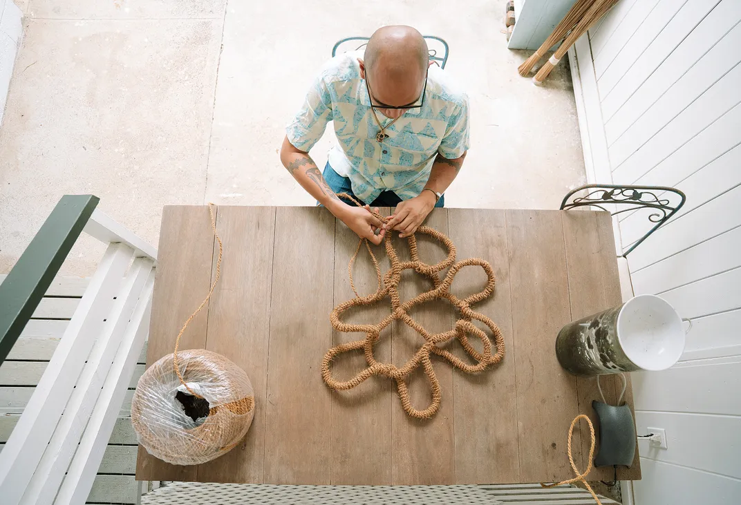 a man is shown from above working on knotting threaded bark