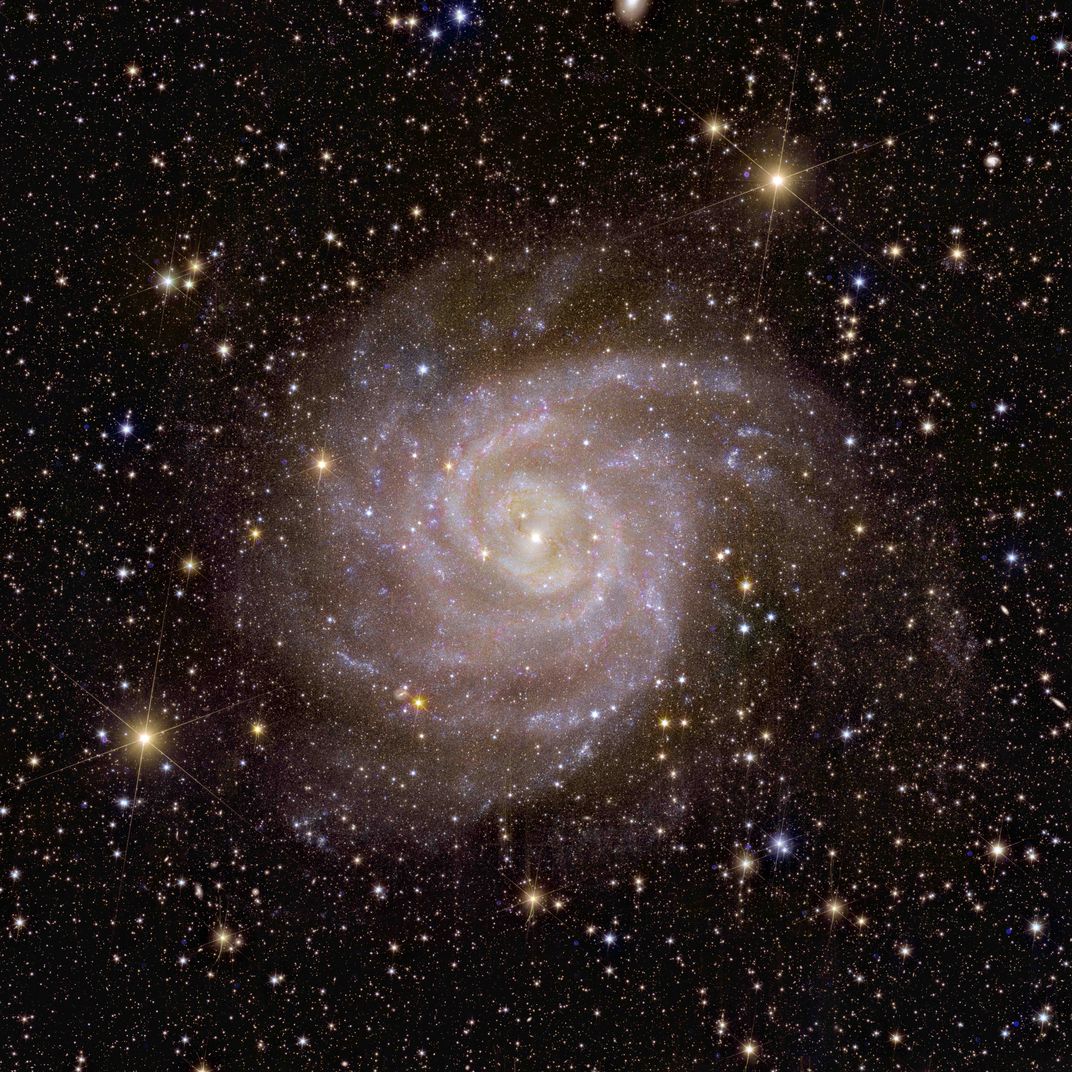 A spiral-shaped galaxy against a backdrop of fainter stars and galaxies and the darkness of space