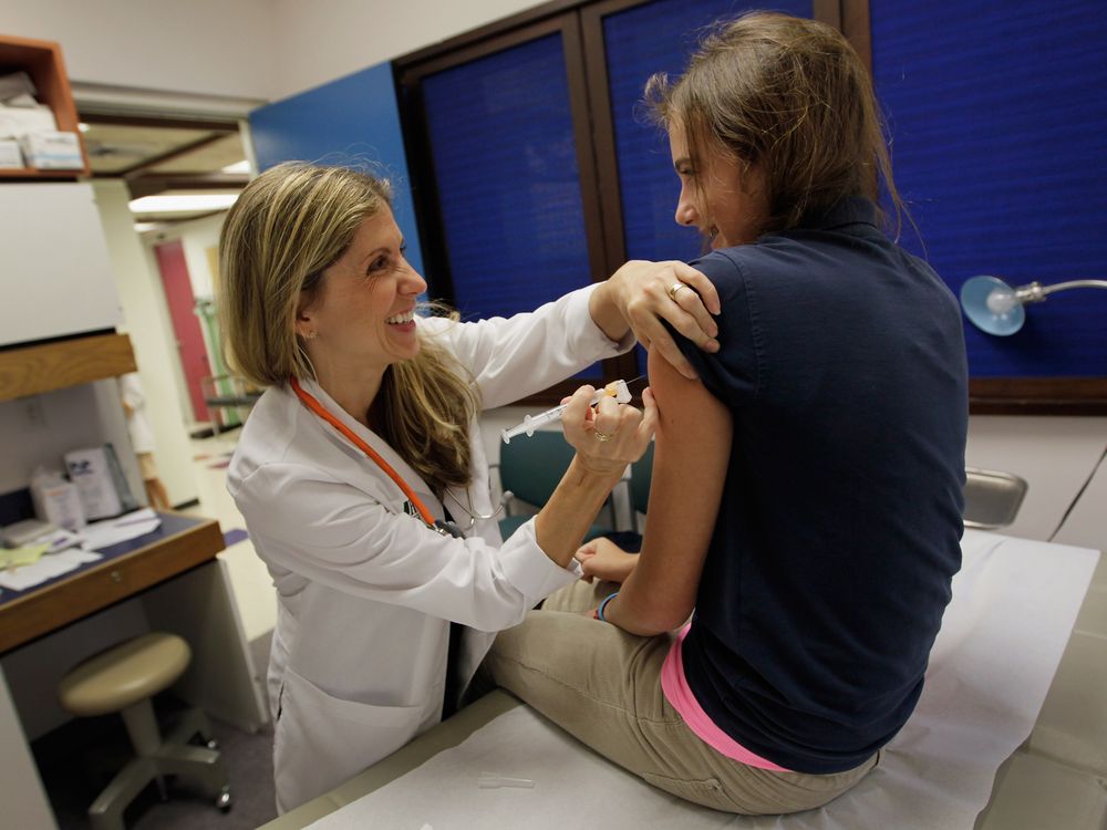 An image of a pediatrician giving an HPV vaccination to a young 13 year old girl in a doctor's office. Both subjects are smiling at each other.