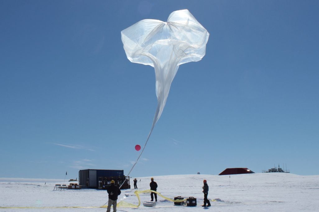 scientists inflate a large white balloon on an icy landscape